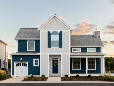 Elmhurst, IL, USA - September 25, 2022: A blue and grey luxury home with a one car garage, covered front porch, and a lake in the background at sunset.